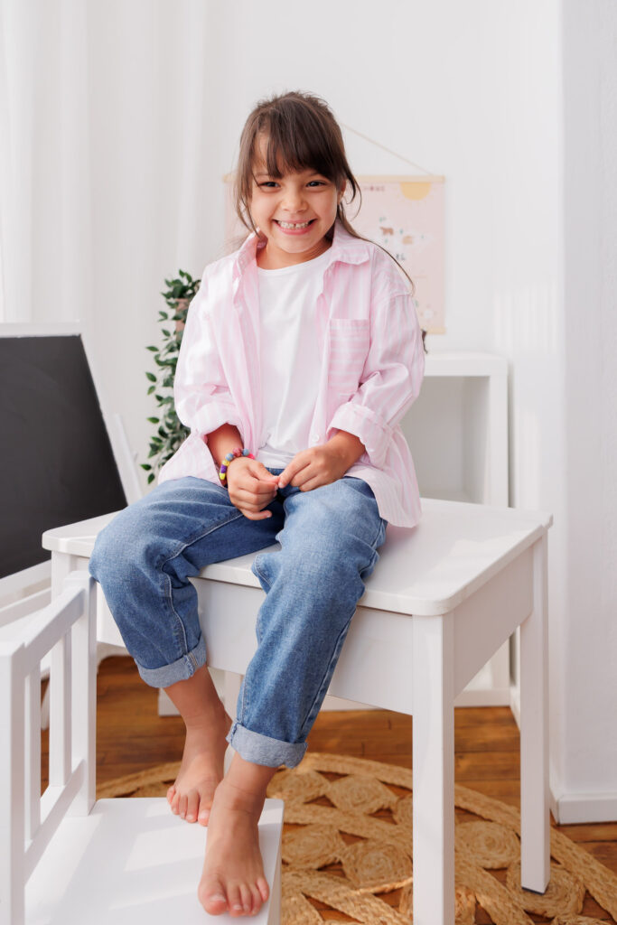 Mädchen sitzt lächelnd auf einem Hocker in Jeans und weißem Shirt, Back-to-School-Mini-Session im Fotostudio Atelier 95 in Luxemburg