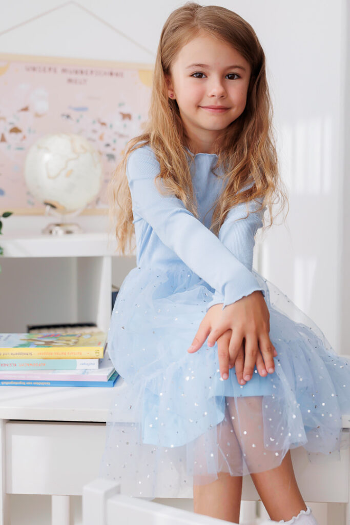 Mädchen sitzt im hellblauen Tüllkleid auf einem Stuhl neben einem Globus, Back-to-School-Mini-Session im Fotostudio Atelier 95 in Luxemburg