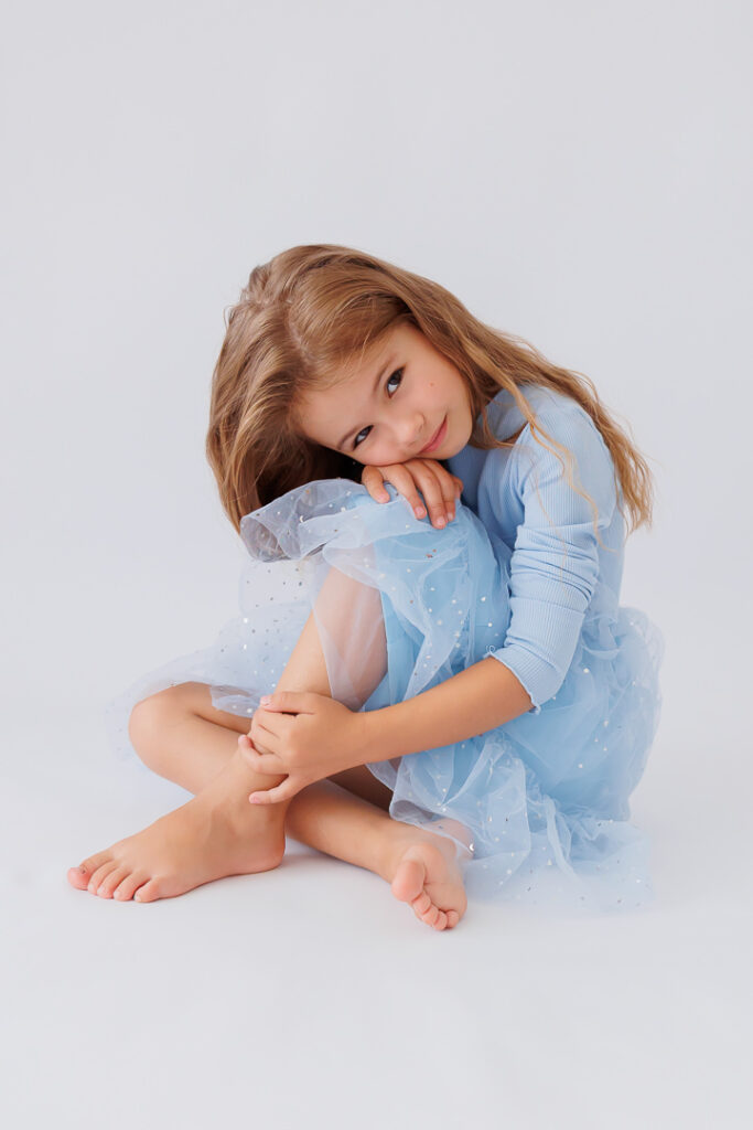 Mädchen sitzt zusammengekauert mit dem Kopf auf den Knien im hellblauen Tüllkleid, Back-to-School-Mini-Session im Fotostudio Atelier 95 in Luxemburg