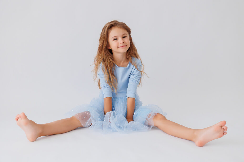 Mädchen sitzt breitbeinig lächelnd auf dem Boden im hellblauen Tüllkleid, Back-to-School-Mini-Session im Fotostudio Atelier 95 in Luxemburg