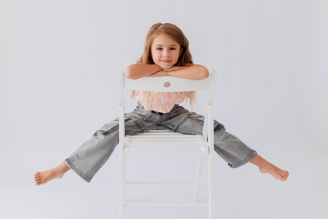 Lächelndes Mädchen stützt die Arme auf eine Stuhllehne und legt den Kopf darauf, Back-to-School-Mini-Session im Fotostudio Atelier 95 in Luxemburg