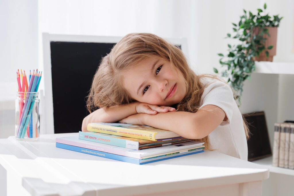 Lächelndes Mädchen legt den Kopf auf verschränkte Arme auf einem Bücherstapel, Back-to-School-Mini-Session im Fotostudio Atelier 95 in Luxemburg
