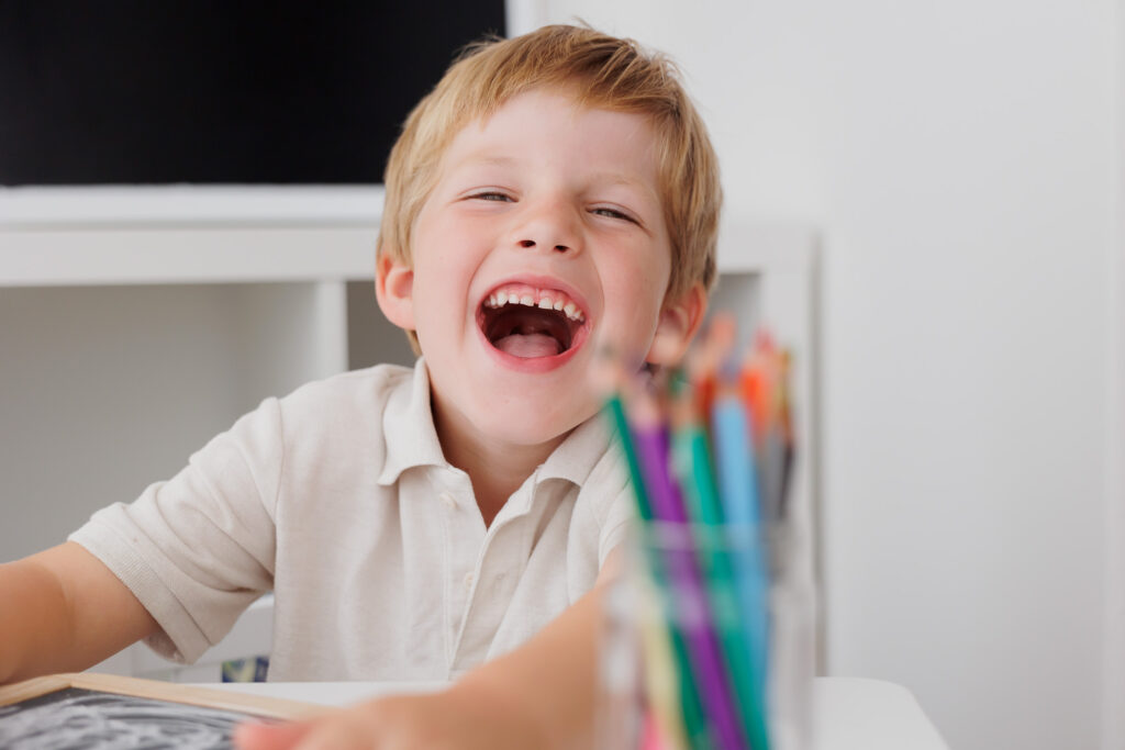 Lächelnder Junge sitzt auf dem Boden mit den Armen um die angezogenen Beine, Back-to-School-Mini-Session im Fotostudio Atelier 95 in Luxemburg