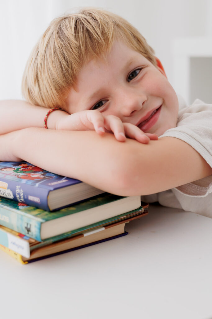 Junge lacht herzhaft mit offenem Mund am Schreibtisch mit bunten Stiften, Back-to-School-Mini-Session im Fotostudio Atelier 95 in Luxemburg