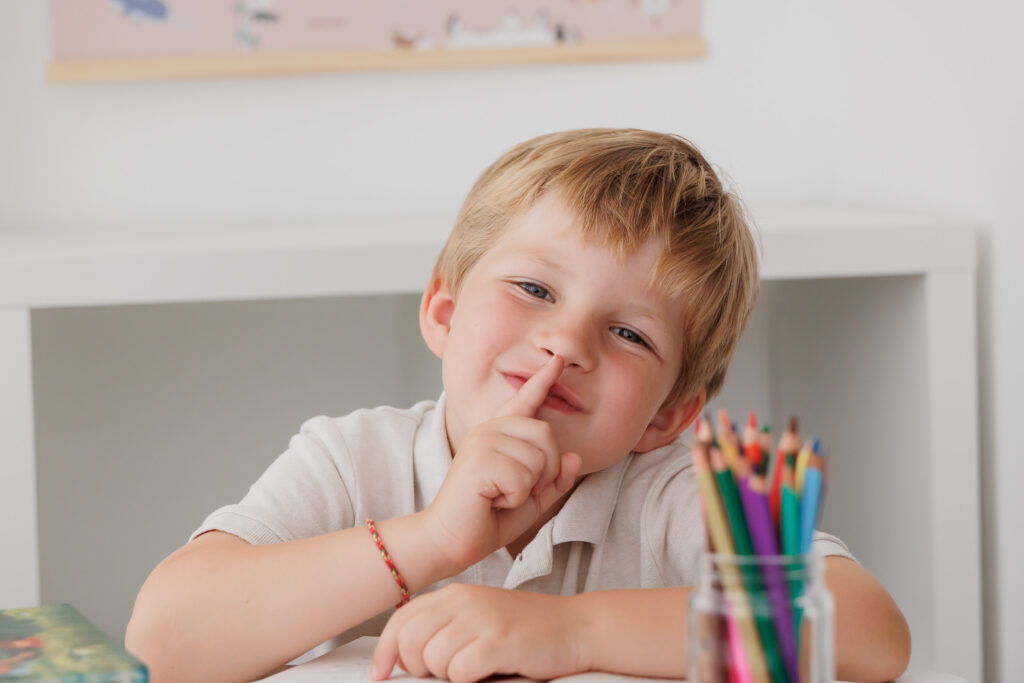 Junge zeigt lächelnd mit dem Finger nach oben an einem aufgeschlagenen Buch, Back-to-School-Mini-Session im Fotostudio Atelier 95 in Luxemburg