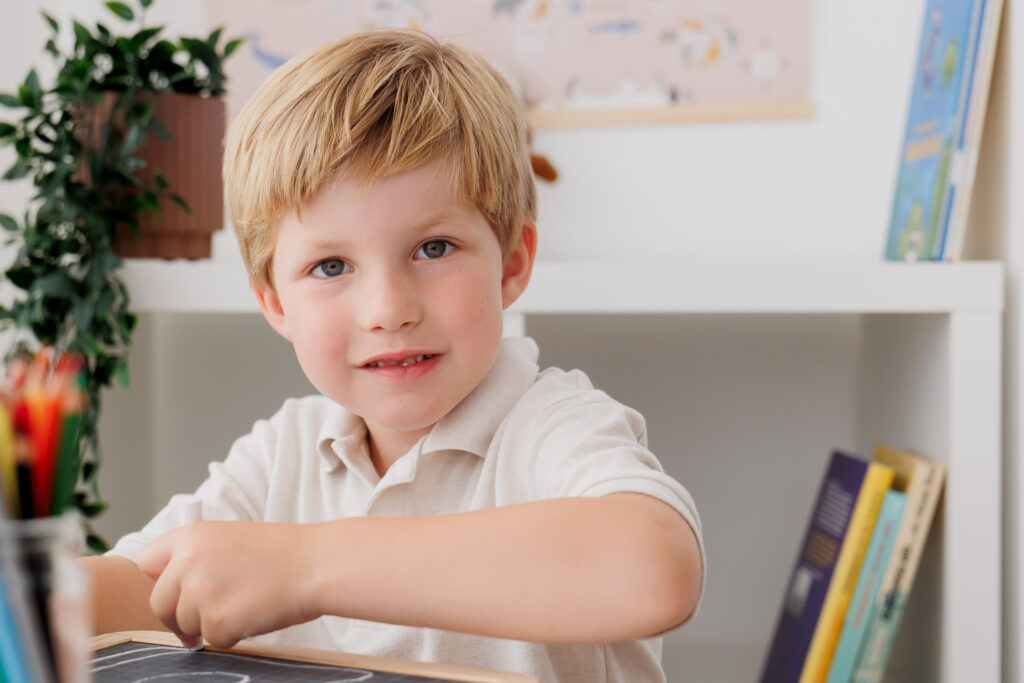 Lächelnder Junge sitzt mit verschränkten Armen am Schreibtisch und blickt zur Seite, Back-to-School-Mini-Session im Fotostudio Atelier 95 in Luxemburg