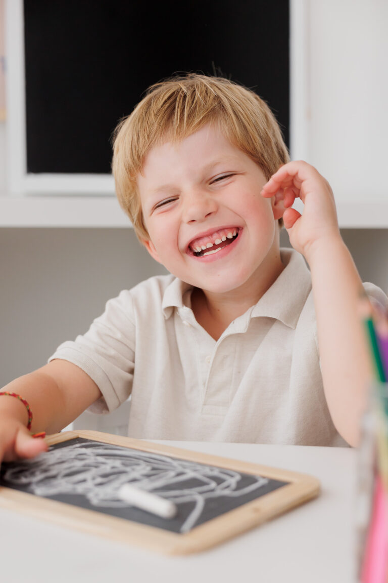 Junge lacht ausgelassen mit der Hand am Kopf vor seiner Schiefertafel, Back-to-School-Mini-Session im Fotostudio Atelier 95 in Luxemburg